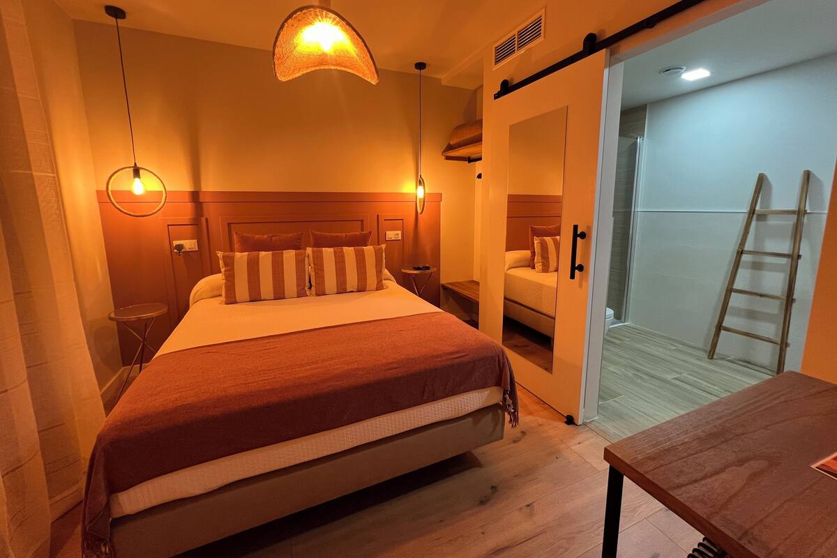 Ein Hotelzimmer mit Bett, Nachttischen, einer Hängelampe und einer Tür zu einem Balkon.