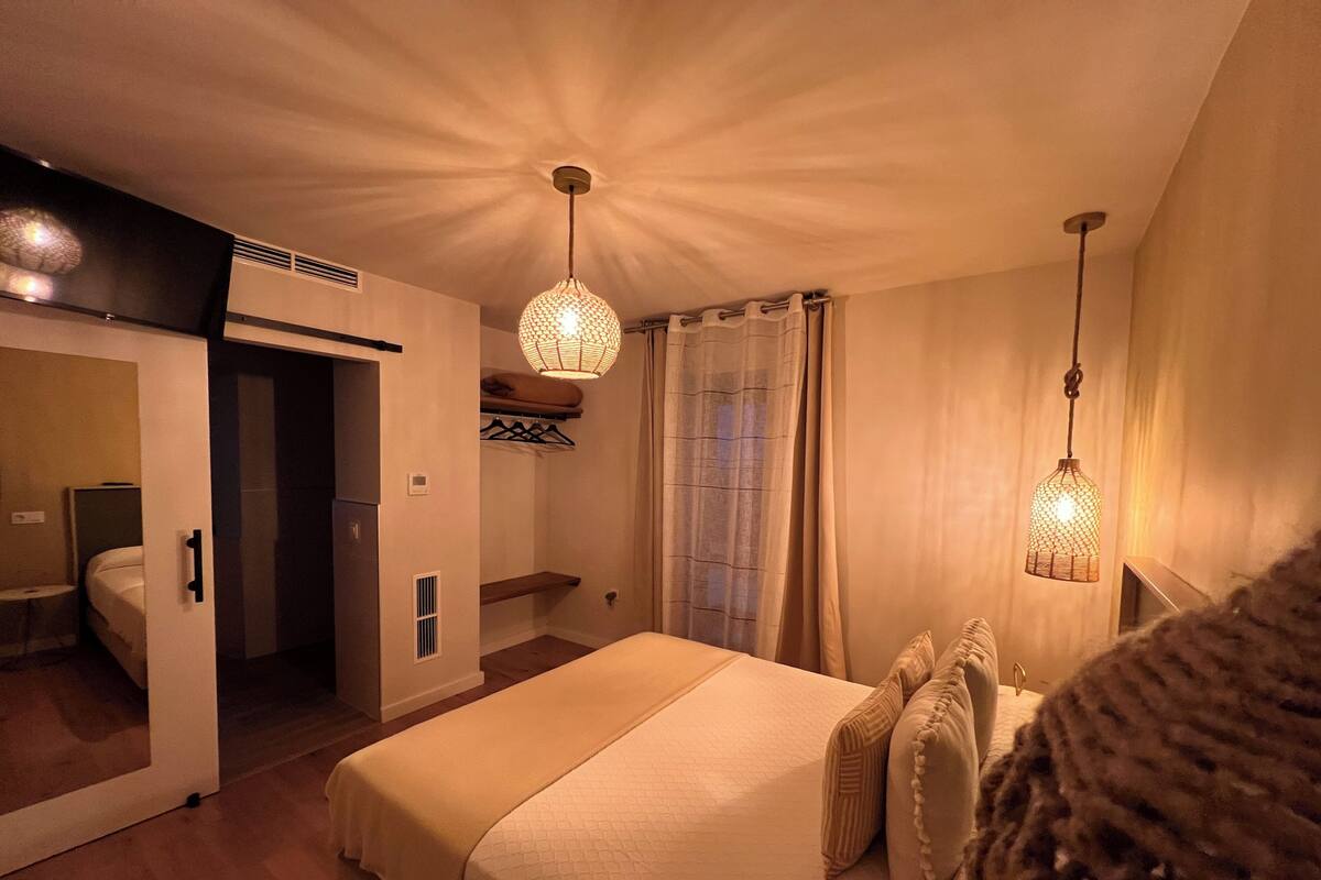 Ein Schlafzimmer mit einem großen Bett, zwei Pendelleuchten, einem begehbaren Kleiderschrank und einem Badezimmer mit Toilette und Waschbecken.