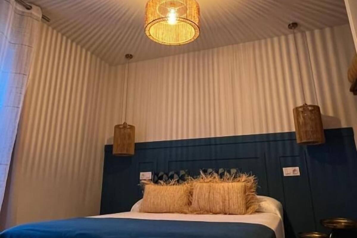 Ein Schlafzimmer mit Bett, einer Pendelleuchte und einem Fenster mit Vorhängen.