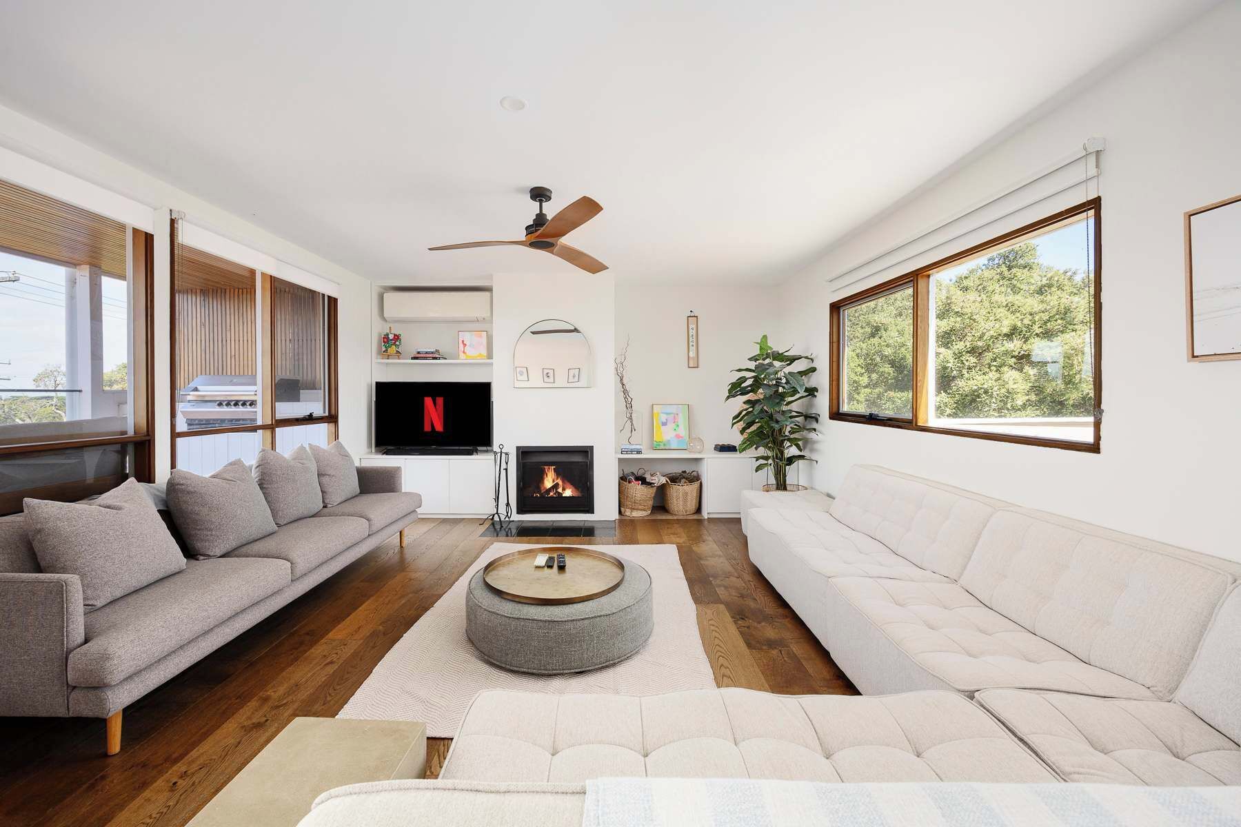A modern living room with a fireplace, a ceiling fan, and large windows.