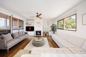 A modern living room with a fireplace, a ceiling fan, and large windows. - Tuckey Terrace | Heated Pool, Spa & Bay Views (Sorrento)