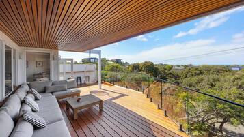 A modern outdoor deck with a wooden ceiling, a sofa set, and a view of the surrounding landscape.