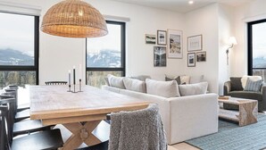 A modern living room with a large wooden table, a sofa, and a hanging light fixture.