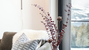 A modern living room with a grey sofa, a clear glass vase with dried flowers, a wooden side table, and a floor lamp.