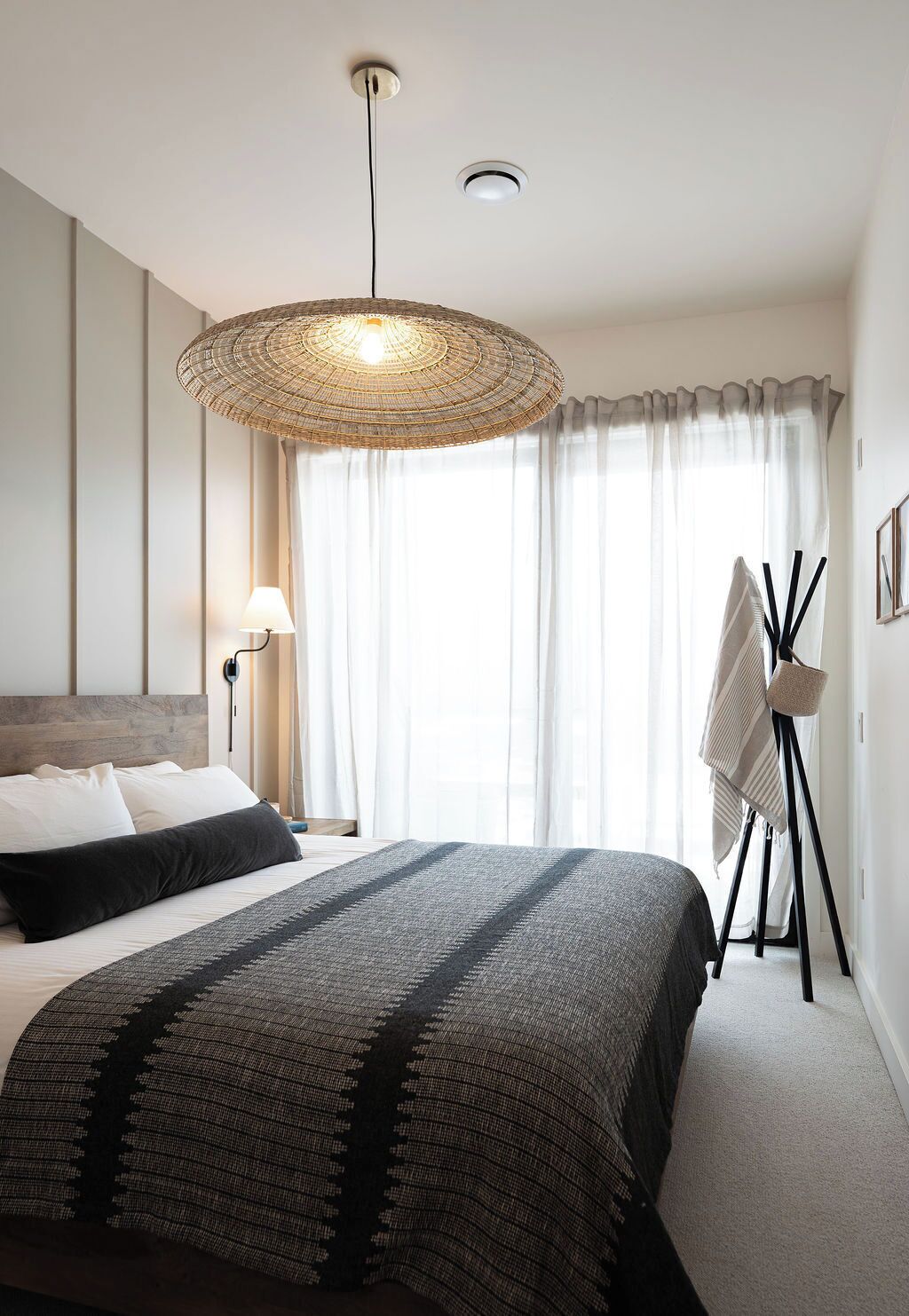 Ein modernes Schlafzimmer mit einem großen Bett, einer Pendelleuchte, einer Nachttischlampe und einem Standventilator.