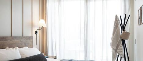 Ein modernes Schlafzimmer mit einem großen Bett, einer Pendelleuchte, einer Nachttischlampe und einem Standventilator.