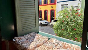 A view from a window with a patterned cushion, a small table, and a plant with red flowers. - Rememorar 01 (Salvador)
