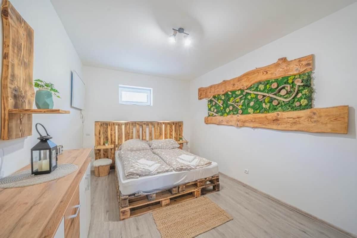 A bedroom with a wooden pallet bed, a rustic wall art piece, a small window, and a wooden nightstand with a lantern.