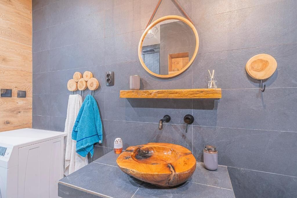 Une salle de bain moderne avec un lavabo en bois, un miroir rond et une étagère en bois.