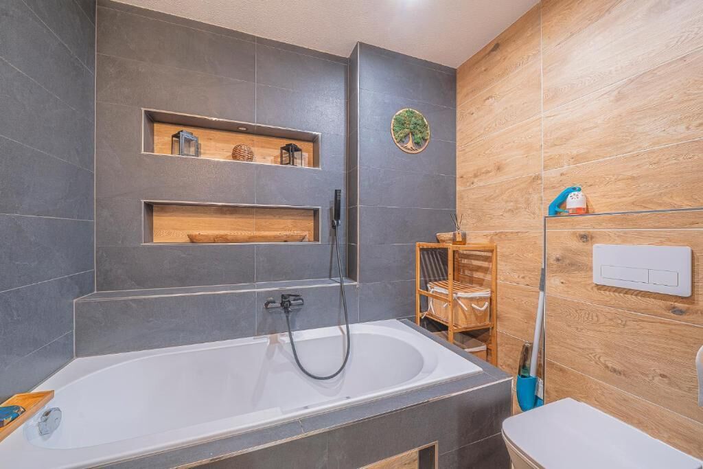 A modern bathroom with a freestanding bathtub, wooden shelves, and a wooden wall panel.