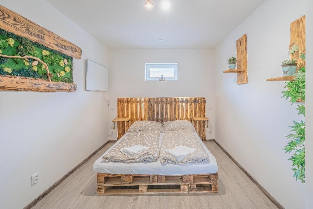 A bedroom with a bed on a wooden pallet, a window with a view, and wooden shelves with plants.