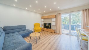 Una sala de estar moderna con un sofá azul, un sillón amarillo, una mesita redonda y un televisor.