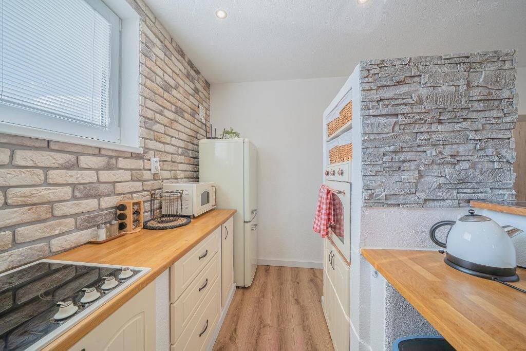 Eine kleine Küche mit Backsteinwand, einem weißen Kühlschrank, einer Mikrowelle, einem Wasserkocher und einer Holzausziehtafel.