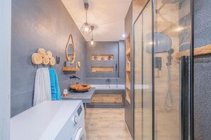 Un baño moderno con cabina de ducha de vidrio, tocador de madera y lavadora integrada.