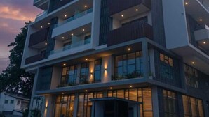 A multi-story hotel with balconies, a ground-level entrance, and a parking area.