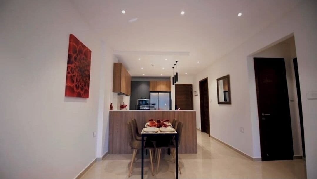 A modern kitchen with a central island, a dining area with a table and chairs, and a hallway leading to a door.