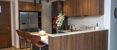 A modern kitchen with wooden cabinets, a stainless steel refrigerator, a central island with bar stools, and pendant lighting.