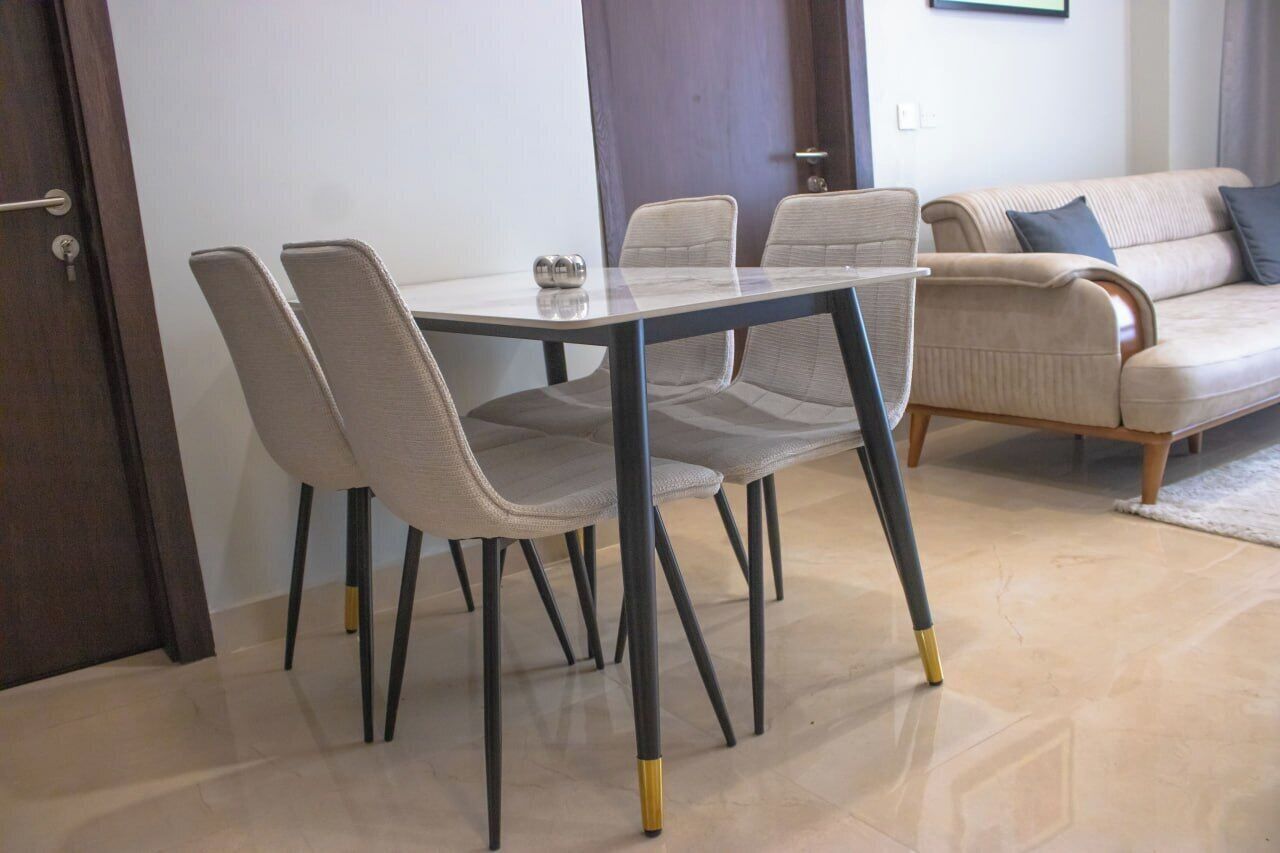 A dining area with a glass table and four chairs, a sofa, and a door.