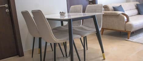 A dining area with a glass table and four chairs, a sofa, and a door.