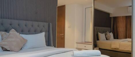 A modern hotel room with a large bed, a bedside table, a mirror, and a sliding door leading to a balcony.