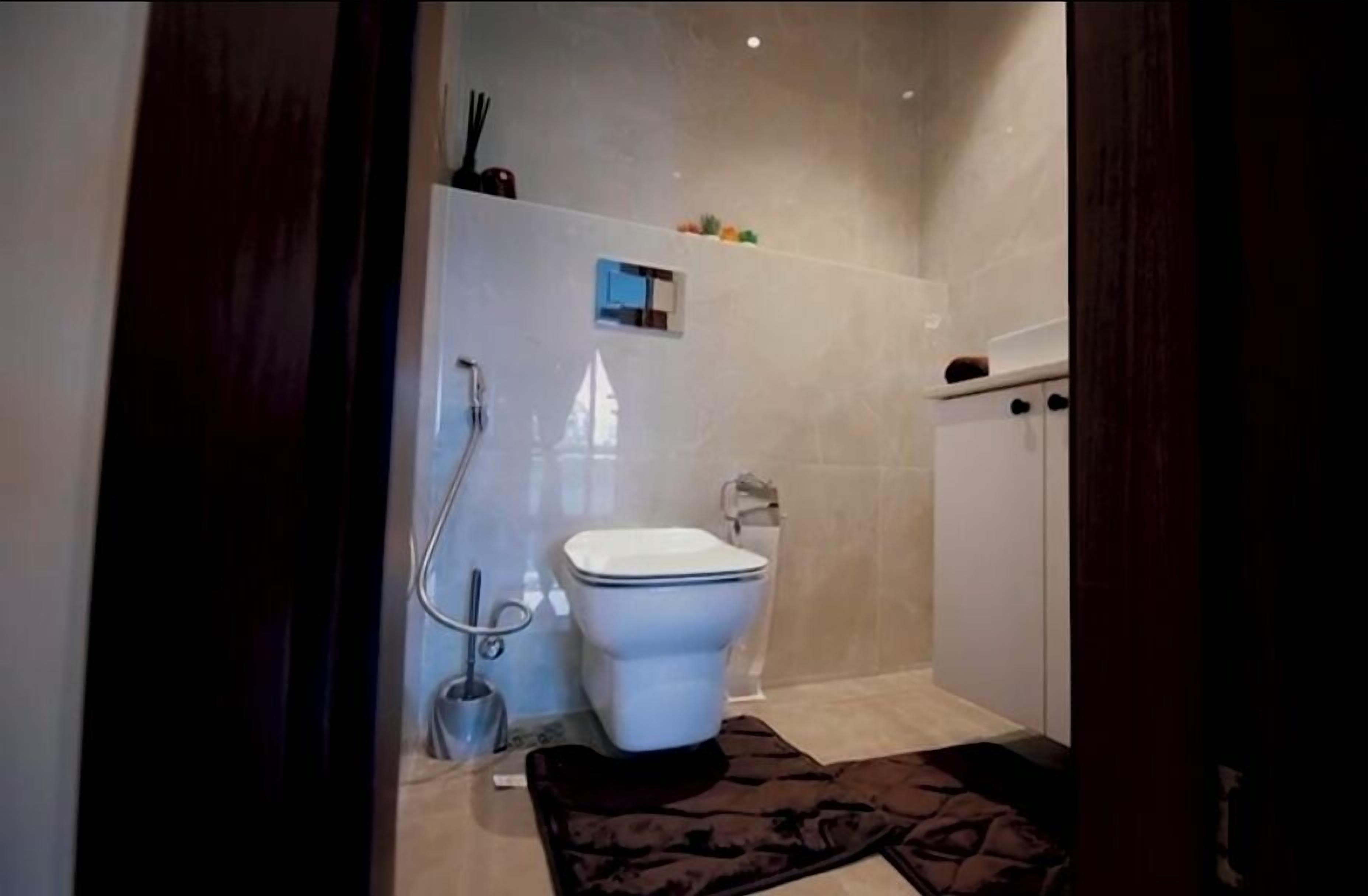 A modern bathroom with a toilet, shower, and a small shelf with toiletries.