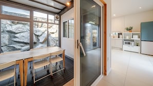 A modern kitchen with a stone wall, a dining area with a table and chairs, and a sliding glass door leading to a balcony. - Gyeongju Awesomeway Pool Villa (Gyeongju)