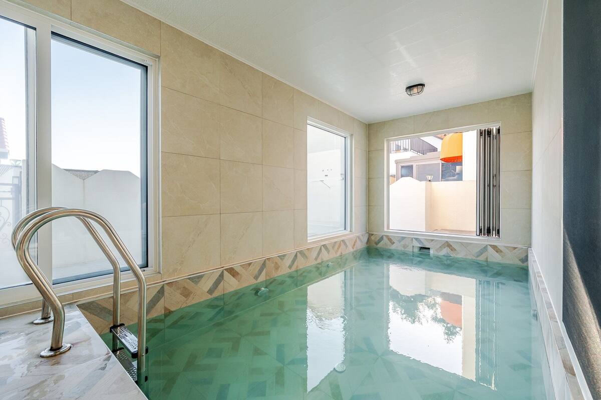 Une piscine à l’eau claire, dotée d’une rampe métallique et de grandes fenêtres.