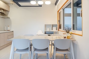 A modern kitchen with a dining area, white cabinetry, and a large window with a view.