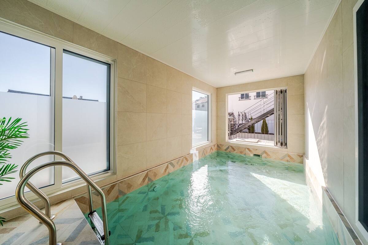 Une piscine à l’eau claire, une échelle en métal et de grandes fenêtres donnant sur l’extérieur.