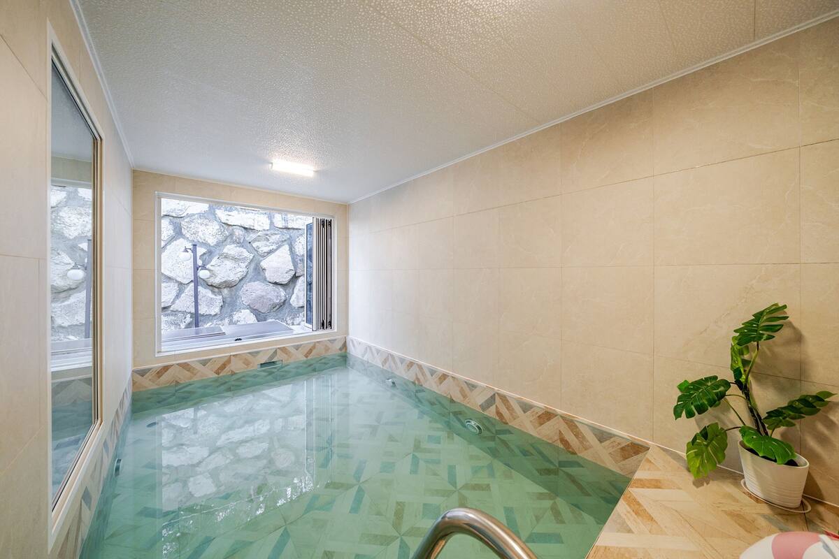 Une salle de spa dotée d’un jacuzzi en verre, d’un mur en pierre et d’une plante en pot.