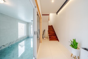 A modern interior with a glass-enclosed pool, a wooden staircase, and a potted plant.
