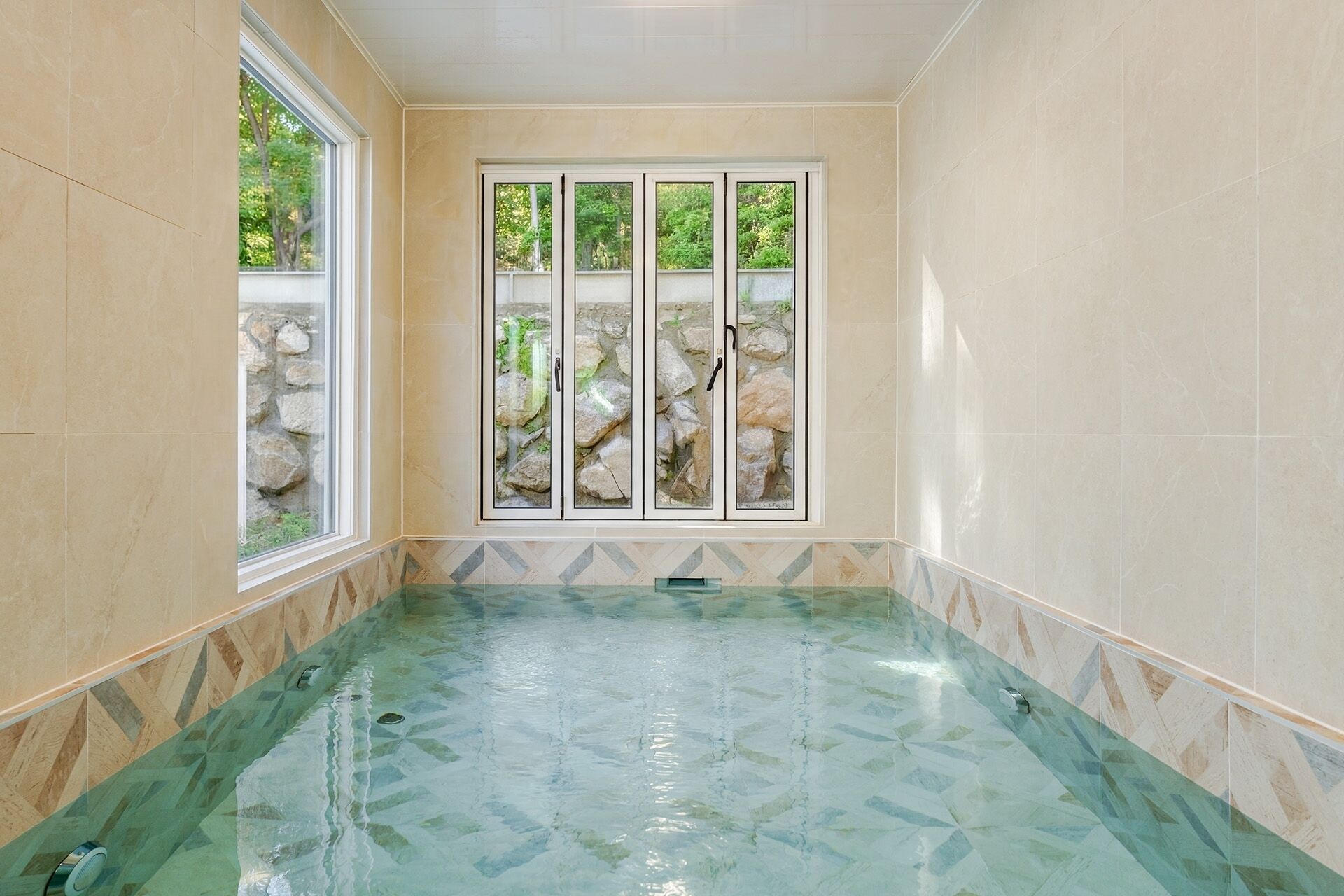 Een wellnessruimte met een glazen hottub, stenen muren en uitzicht op groen.