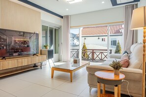A modern living room with a TV, sofa, coffee table, and a balcony with a view of buildings.