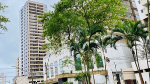 Un edificio moderno de gran altura con varios balcones, rodeado de vegetación y un sendero adoquinado.