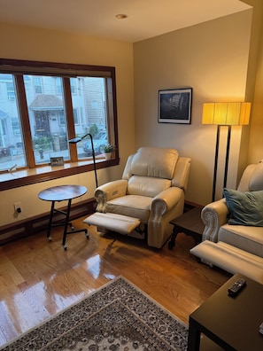 Un saló amb un finestral gran, un butac armchair de pell, un sofà, una taula petita i una làmpada de peu.