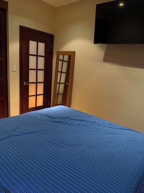 Un dormitorio con cama, una puerta y televisor montado en la pared.
