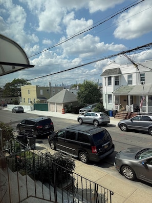 Une rue résidentielle bordée de voitures garées, une maison avec un porche et un ciel dégagé.