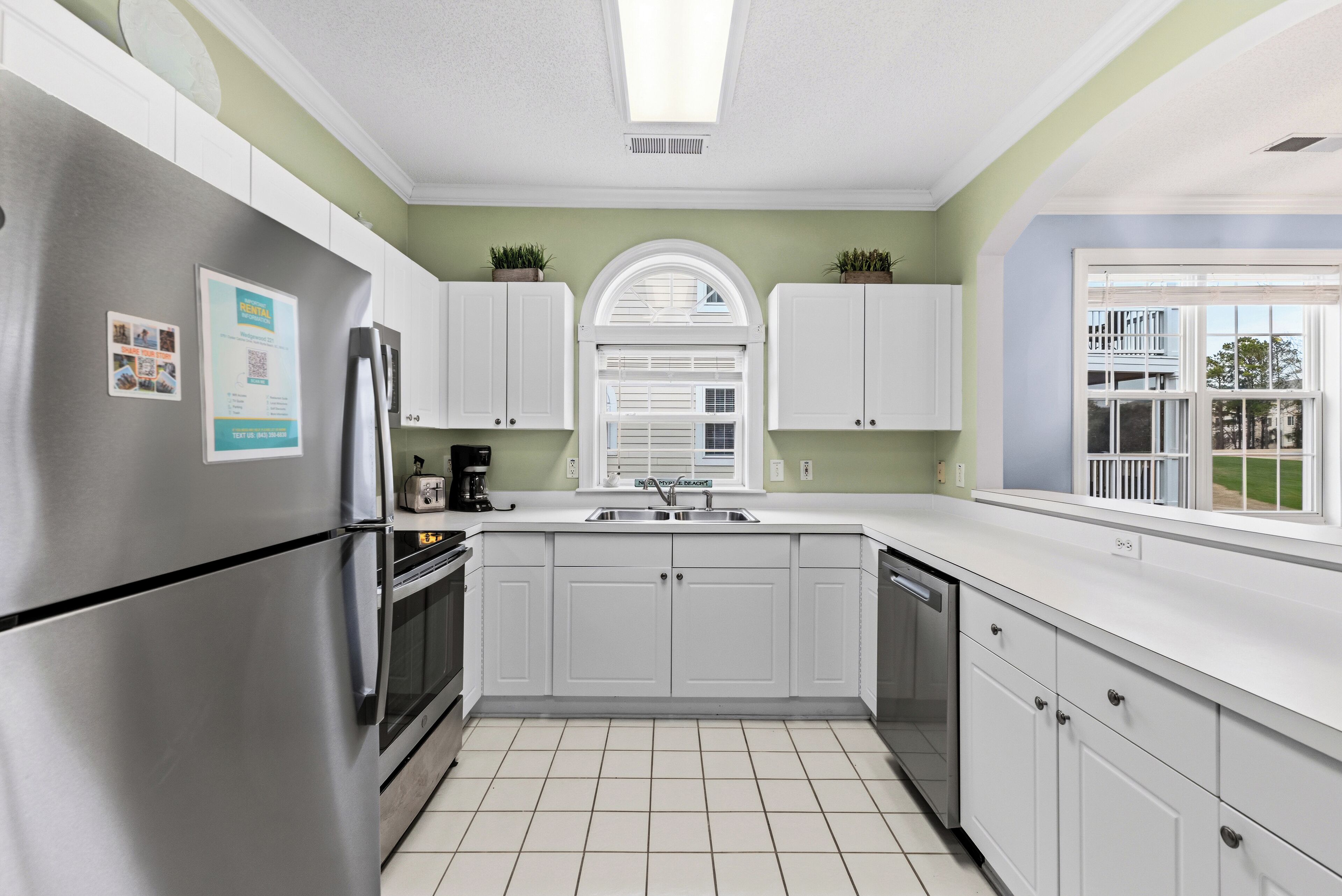 A modern kitchen with white cabinets, stainless steel appliances, and a window with a view of the outside.