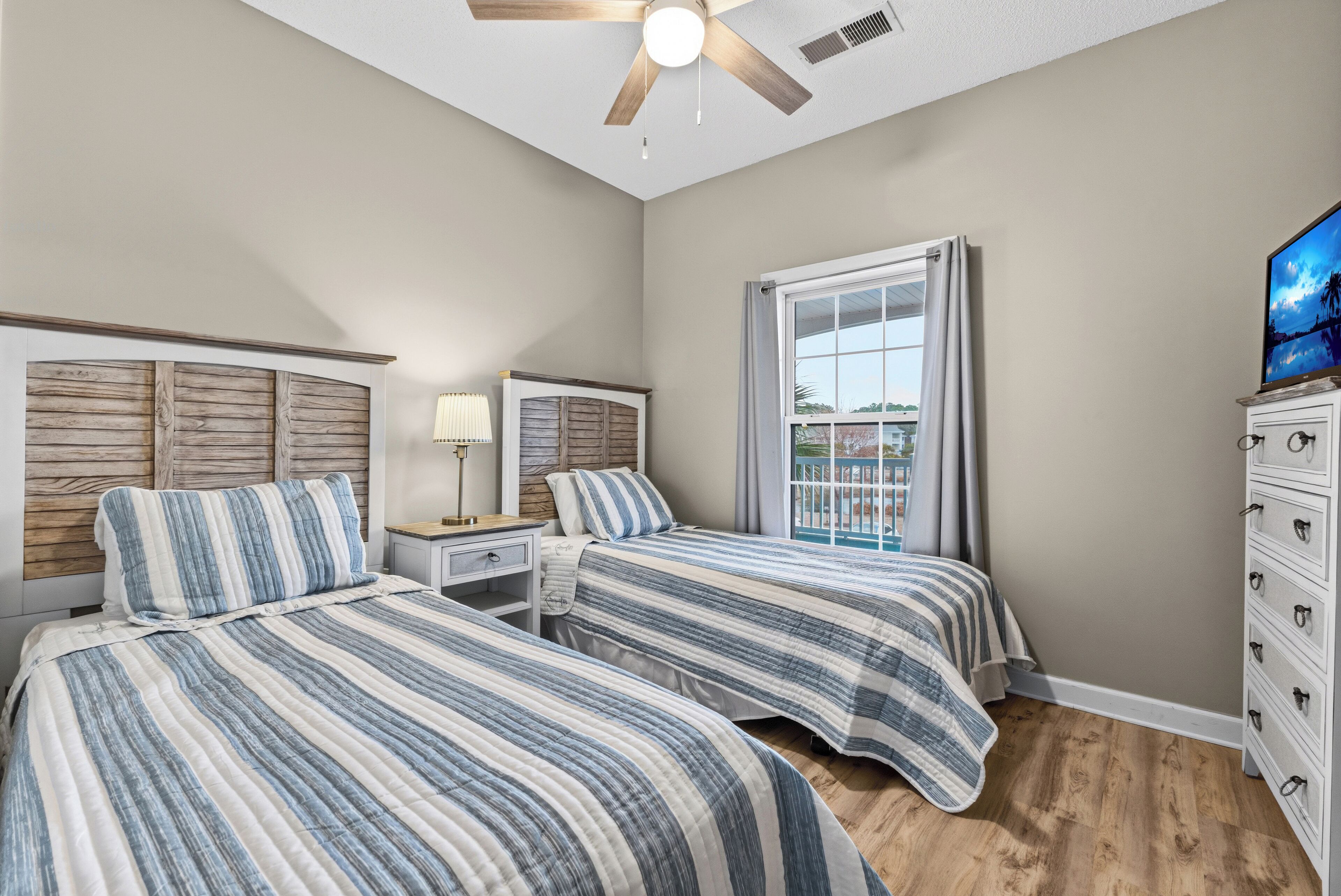 A bedroom with two beds, a ceiling fan, a window with curtains, and a dresser.