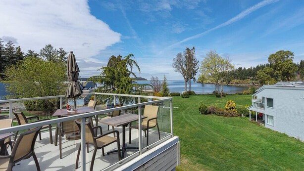 Une terrasse dotée de mobilier d’extérieur, offrant une vue sur un lac, une pelouse verdoyante et une maison.