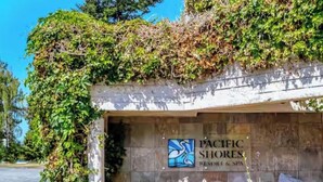 Une enseigne pour le Pacific Shores Resort & Spa, avec son logo, entourée de verdure et sous un ciel dégagé.