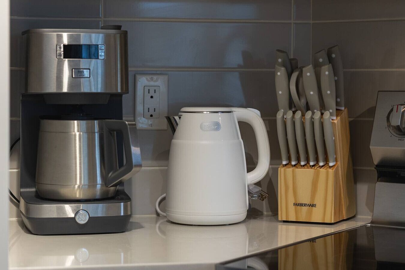 Una cocina con cafetera, hervidor y bloque de cuchillos.