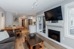 Un salon moderne doté d’un téléviseur à écran plat, d’une cheminée, d’un coin repas et d’une cuisine.