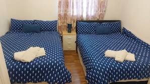 A room with two beds, each with a blue patterned bedspread and matching pillows. There is a wooden nightstand with a lamp between the beds. - Citylink 2-bedroom flat, 8 mins to London bridge. Sleeps 7. (London)