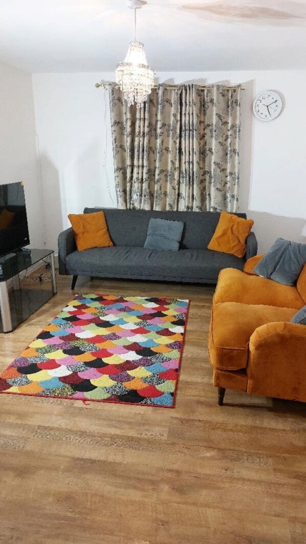 A living room with a sofa, a colorful rug, a television, and a chandelier. - Citylink 2-bedroom flat, 8 mins to London bridge. Sleeps 7. (London)