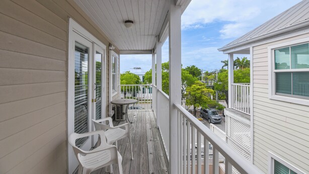 A covered porch with a table and chairs, a view of the street, and a building with a balcony. - Casa Havana | Old Town Condo w/ Pool & Balcony (Key West)