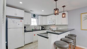 A modern kitchen with white cabinets, a built-in microwave, a refrigerator, a sink, and bar stools. - Casa Havana | Old Town Condo w/ Pool & Balcony (Key West)