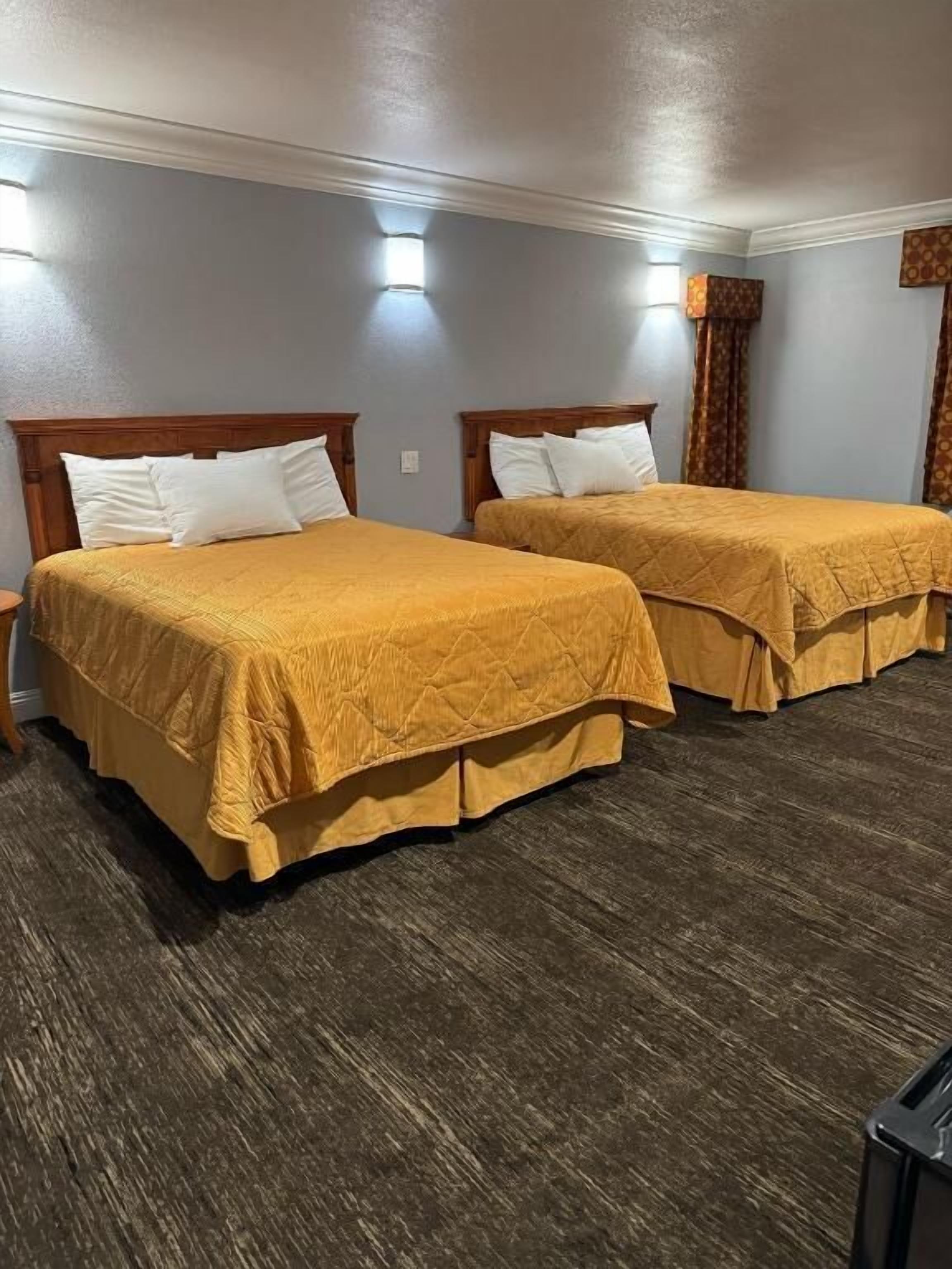 Quarto de hotel com duas camas, cabeceiras de madeira e chão de madeira escura.