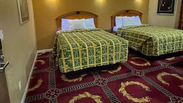 A hotel room with two beds, each with a patterned bedspread, a red carpet with geometric designs, and wall-mounted lights.