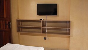 Een kamer met een tv aan de muur, een houten plank eronder en een deur links.